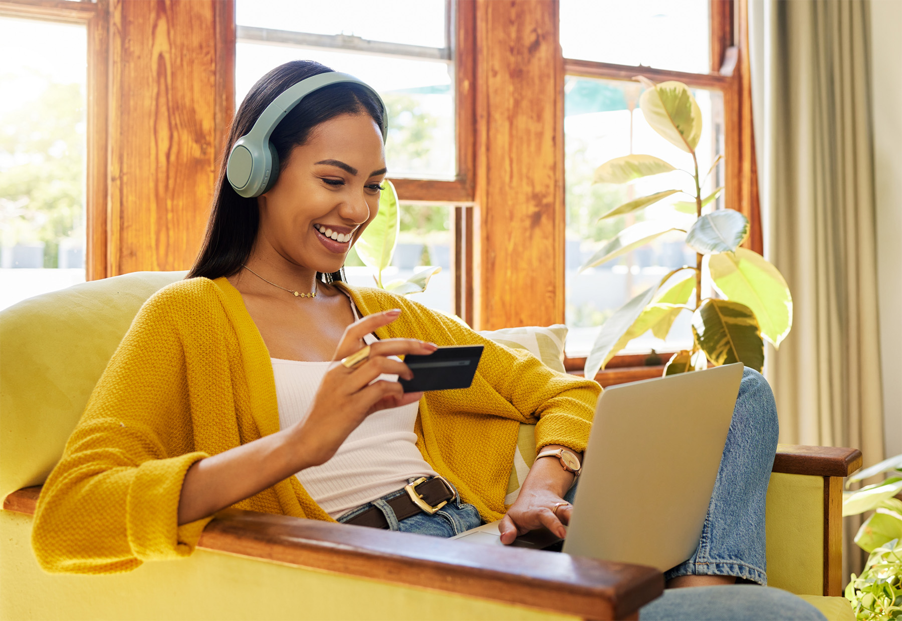 woman holding a card while using a laptop with headphones